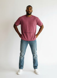 BubiniSegreti T-Shirt in Beeren-Ton mit geprägtem Textdesign, getragen von einem Mann mit Jeans und weißen Sneakern.
