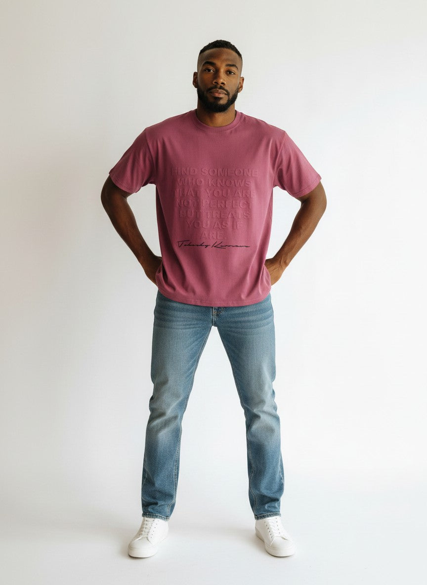 BubiniSegreti T-Shirt in Beeren-Ton mit geprägtem Textdesign, getragen von einem Mann mit Jeans und weißen Sneakern.