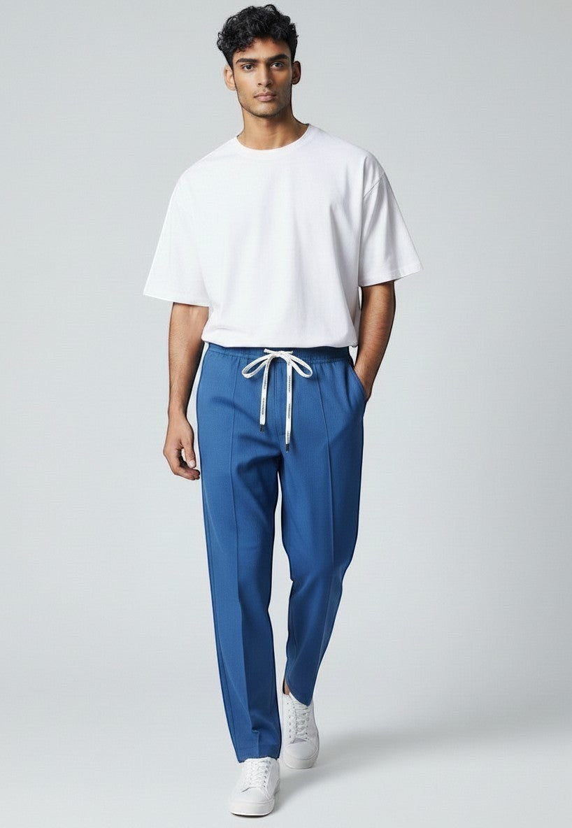 BubiniSegreti blaue Stoffhose für Herren mit Kordelzug und Bügelfalte, kombiniert mit weißem T-Shirt und Sneakern.