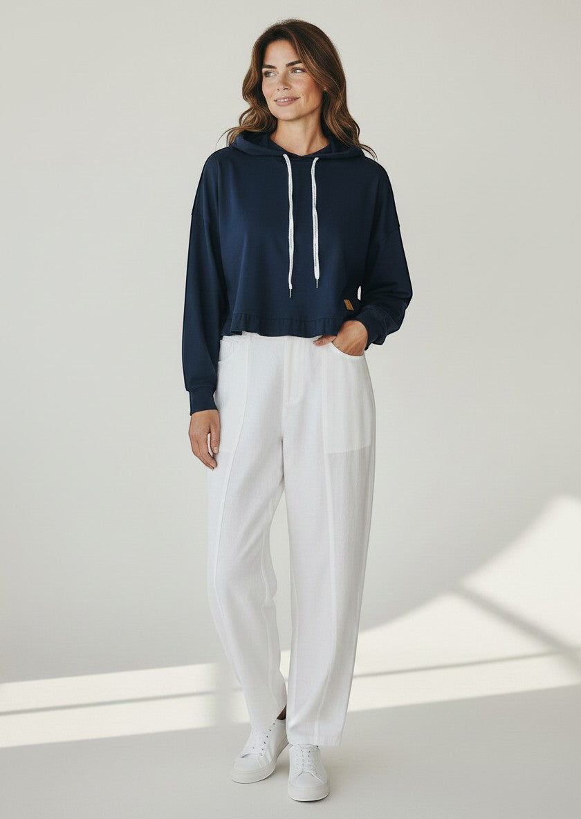 BubiniSegreti dunkelblauer Cropped-Hoodie mit weißen Kordelzügen und goldenem Logo, getragen von einer Frau mit weißer Hose