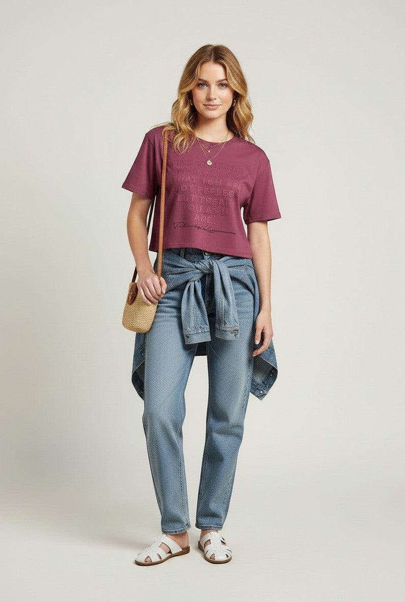 BubiniSegreti kurzes T-Shirt in Beerenton mit geprägtem Schriftzug, getragen von einem Model mit Jeans und Sandalen.
