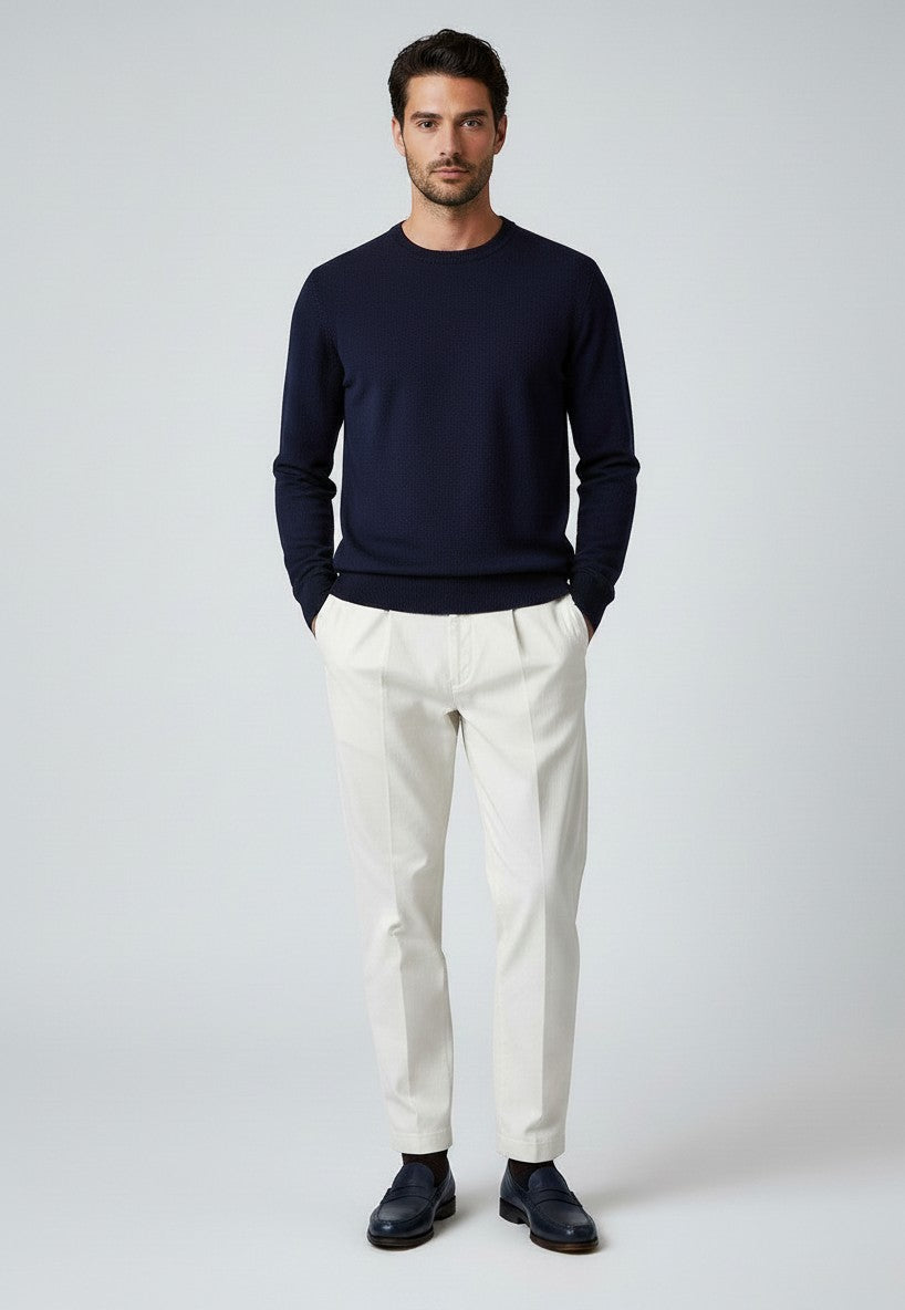 BubiniSegreti Herren-Stoffhose in Off-White mit Bundfalten, kombiniert mit dunkelblauem Pullover und Loafern.