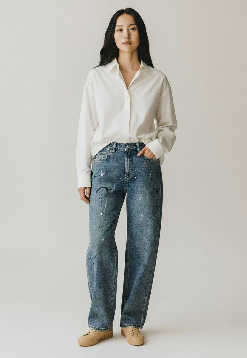 BubiniSegreti weite Jeans mit Paint-Splatter-Design in Blau, getragen von Model mit weißem Hemd und Sneakern.